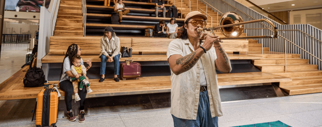 Musician plays an instrument at PDX as passengers sit in the background.